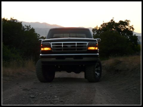 1996 Ford Bronco - Front view of a black 1996 Ford Bronco parked on a dirt road at dusk.