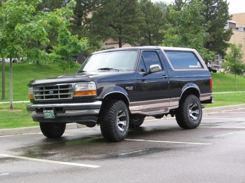 1996 Ford Bronco - This 1996 Ford Bronco is parked in a lot with trees and a building in the background.