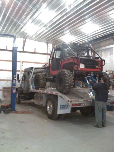 1992 Ford Bronco - A red off-road vehicle with a custom roll cage is loaded onto a flatbed truck inside a garage.