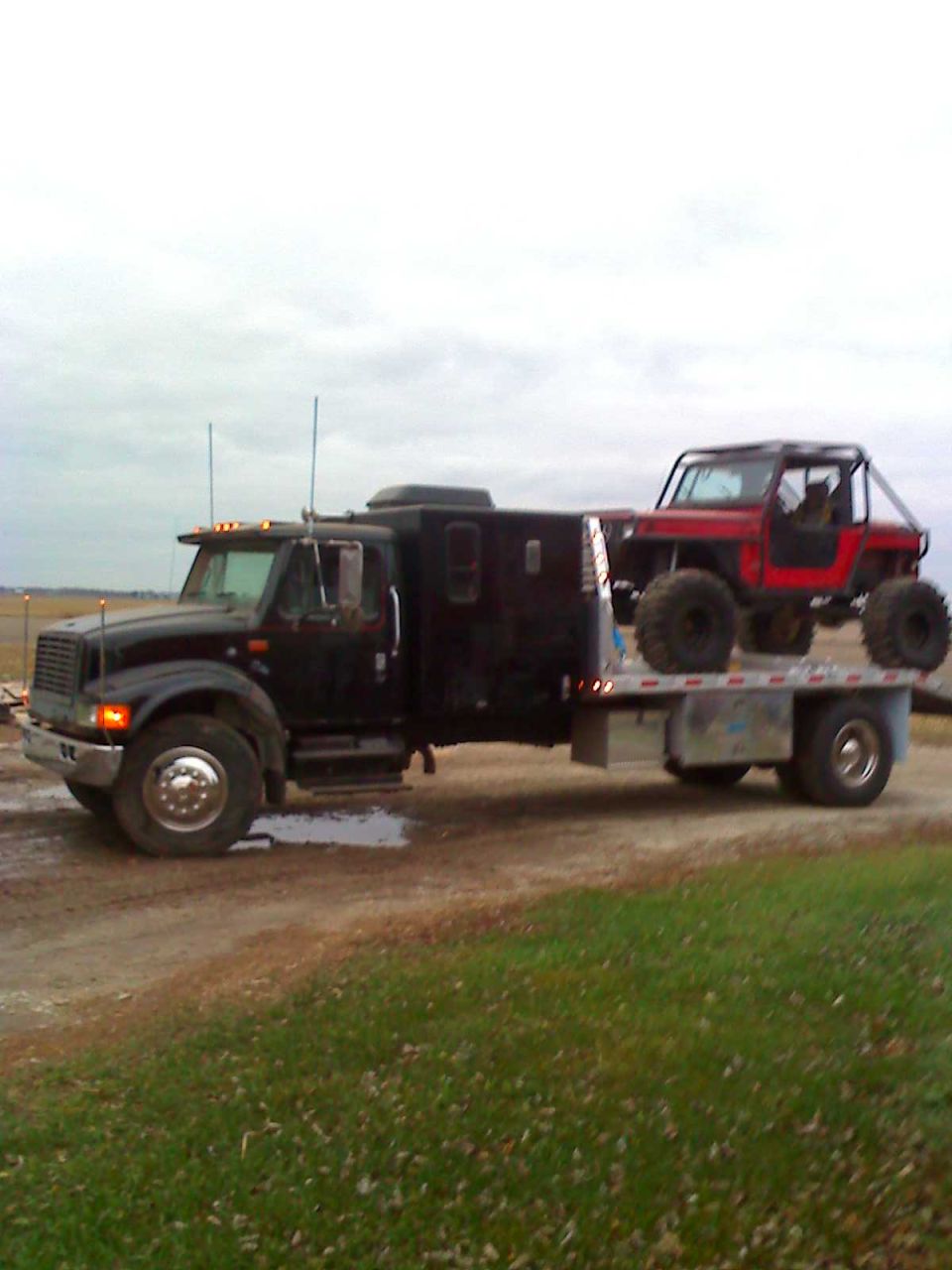 Flatbed truck carrying a red off-road vehicle. The truck has a custom box on the back