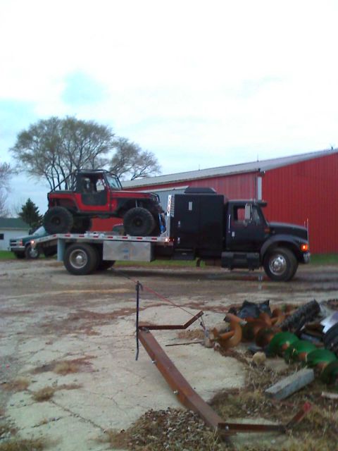 1992 Ford Bronco - A red Jeep is loaded onto a flatbed trailer pulled by a black semi-truck.