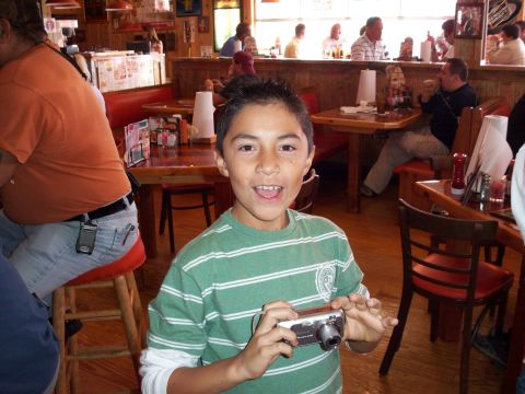 1996 Ford Bronco - A young boy smiles while holding a digital camera in a busy restaurant setting.