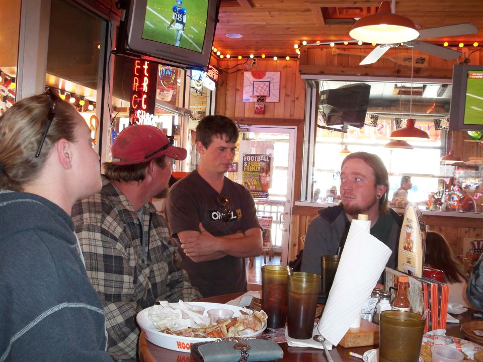 Four people sit at a table in a restaurant, with TVs on the wall showing football