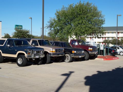 1996 Ford Bronco - Several Ford Broncos and trucks are parked in a lot on a sunny day. The vehicles are lined up facing forward.