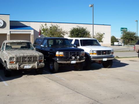 1996 Ford Bronco - Three trucks are parked in a lot on a sunny day. The white truck in the foreground appears to be a 1996 Ford Bronco.