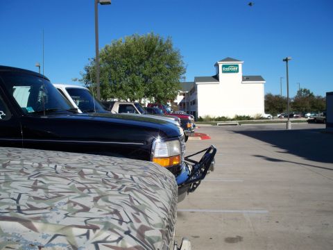 1996 Ford Bronco - Several trucks are parked in a lot with a hotel in the background under a clear blue sky.