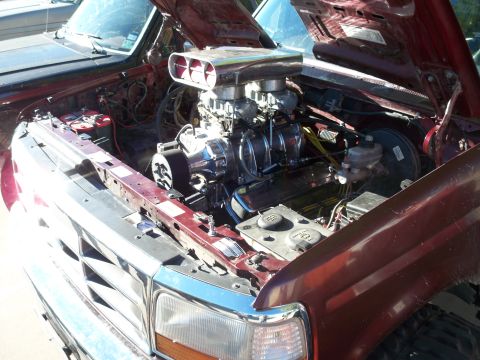 1996 Ford Bronco - The engine bay of a vehicle features a prominent supercharger and custom modifications, with another vehicle in the background.