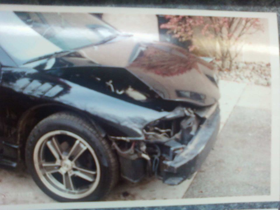Front corner of a black car with significant damage to the front bumper and hood