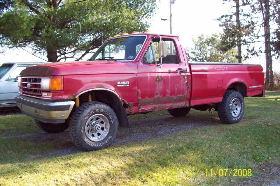 1989 Ford F-150 pickup truck, red, with rust on doors and fenders