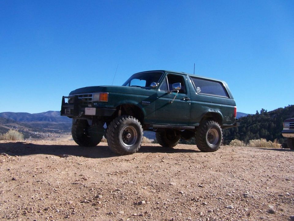 Green Ford Bronco with lifted suspension and off-road tires parked on a dirt hill