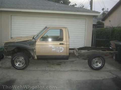 1990 Ford Bronco - side view of a tan project pickup truck showing exposed rear frame rails and missing bed, parked on big tires in a driveway.