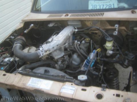 1990 Ford Bronco - open engine bay of a tan vehicle reveals an inline fuel-injected engine, intake plenum, brake master cylinder and a California windshield s…