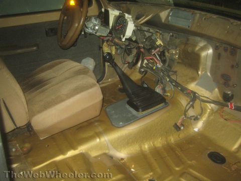 1990 Ford Bronco - stripped vehicle interior shows a steering wheel, exposed gauge cluster, manual shifter boot and a single seat over a bare painted floor pa…