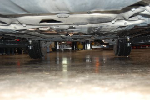 2002 BMW M3 - The underside of a car is visible, supported by jack stands, with a focus on the tires and the undercarriage components.