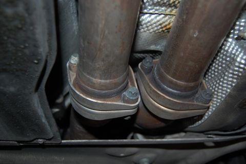 2002 BMW M3 - Close-up view of exhaust pipe connections underneath a vehicle, with a website logo in the corner.