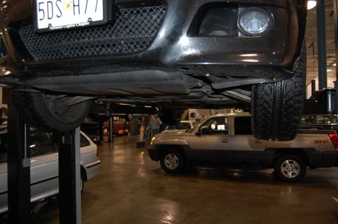 2002 BMW M3 - The underside of a black car is shown on a lift, with a silver pickup truck in the background. The license plate is visible.