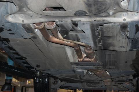 2002 BMW M3 - The undercarriage of a vehicle, with exhaust components and protective panels visible, is shown from below.