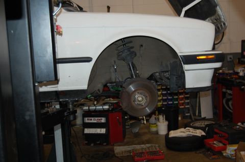 2002 BMW M3 - A white car is on a lift with its front wheel removed, revealing the suspension and brake components.