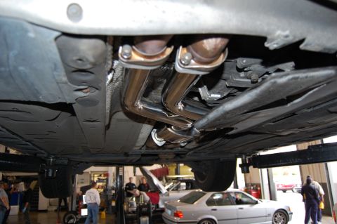 2002 BMW M3 - The underside of a vehicle shows a shiny new exhaust system, with other cars in the background.