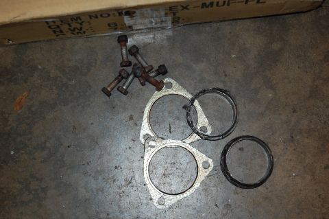 2002 BMW M3 - A collection of exhaust gaskets and bolts are laid out on a concrete surface, with a cardboard box in the background.