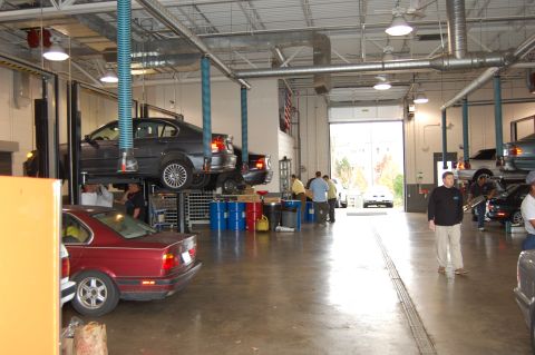 2002 BMW M3 - Several cars are in a repair shop, with one BMW M3 elevated on a lift.