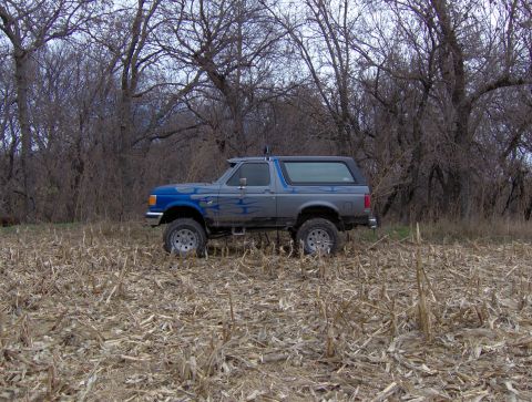 1987 Ford Bronco - This 1987 Ford Bronco is captured in a side profile, parked in a field with dry corn stalks and bare trees.
