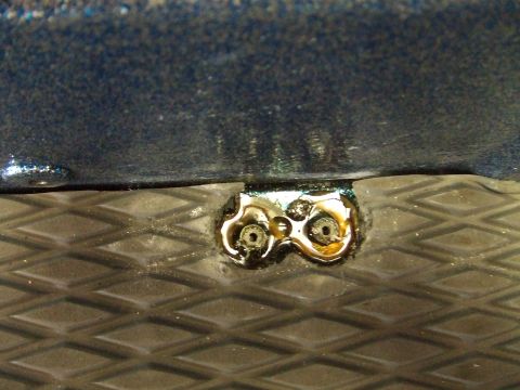 1998 Kawasaki JH1100-A4 1100 ZXi - Close-up view of a metal bracket with two bolts attached to a blue hull, resting on a textured surface.