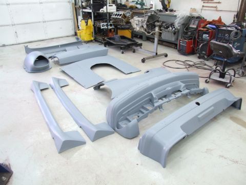 1990 Ford Mustang - Various unpainted car body panels are arranged on the floor of a garage, with an engine and tools in the background.