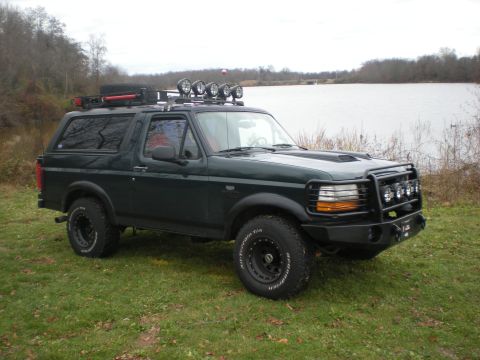 1993 Ford Bronco - This 1993 Ford Bronco features a custom front bumper, roof rack, and auxiliary lights, parked by a lake.