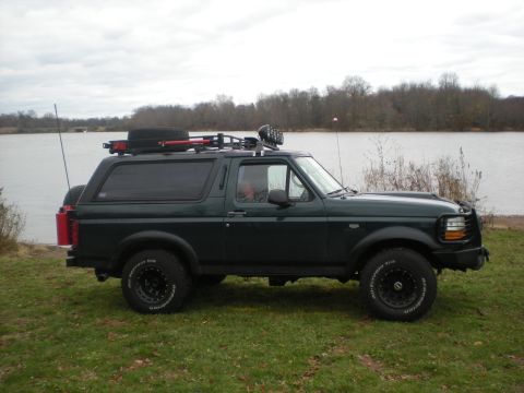 1993 Ford Bronco - Side view of a dark green 1993 Ford Bronco parked outdoors near a lake with trees in the background.