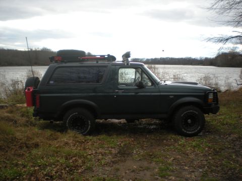 1993 Ford Bronco - This Ford Bronco is parked near a body of water with trees in the background under an overcast sky.