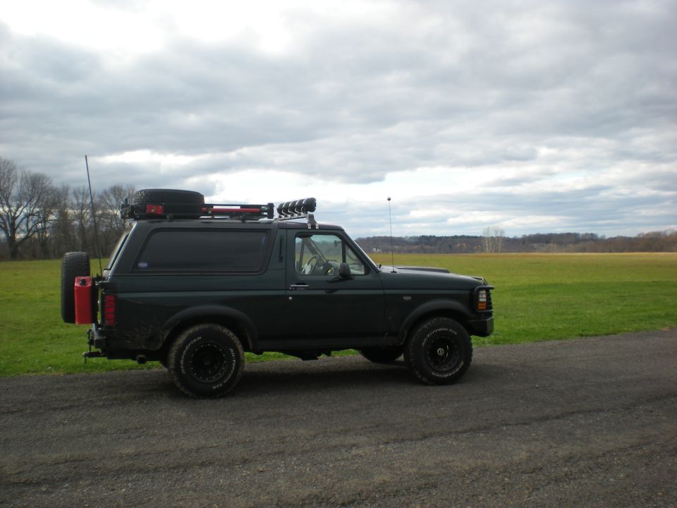 Dark green 1993 Ford Bronco side view with roof rack and spare tire
