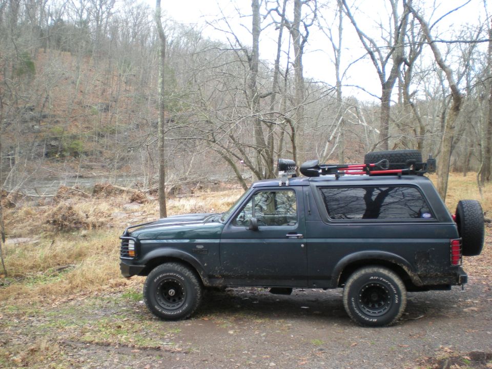 Dark green Ford Bronco parked off-road with roof rack and spare tire.