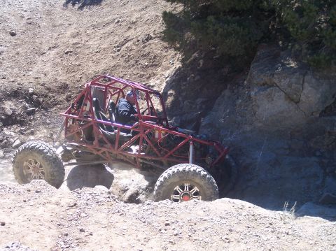 1995 Ford Bronco - A red tube-frame off-road buggy with a driver navigates a rocky, dirt trail.