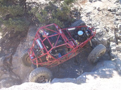 1995 Ford Bronco - A red off-road buggy with large tires is navigating a steep, rocky incline with a driver visible inside. The buggy appears to be mid-climb,…
