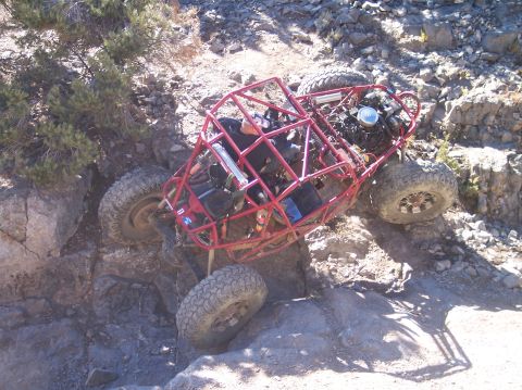 1995 Ford Bronco - A red tube chassis off-road buggy is tilted precariously on a rocky incline, with its front left tire wedged against a large rock and its r…
