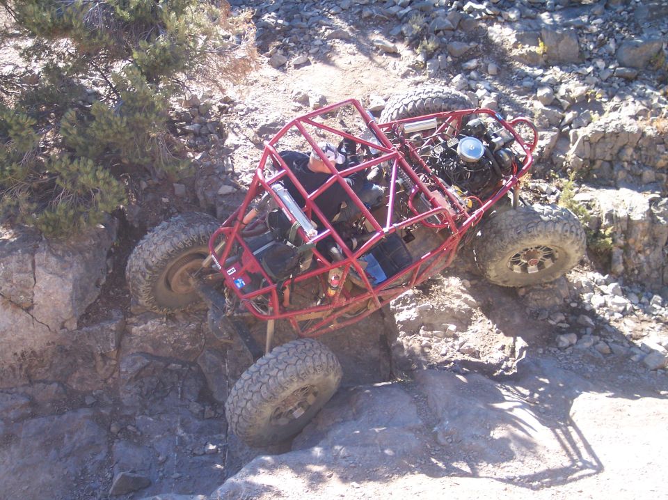 Red tube chassis off-road buggy tilted on a rocky slope.