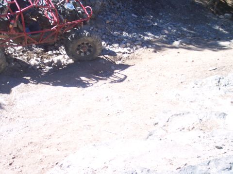 1995 Ford Bronco - The rear tire and suspension of a red off-road buggy are visible on a dirt and rocky trail. The buggy appears to be parked on an incline.