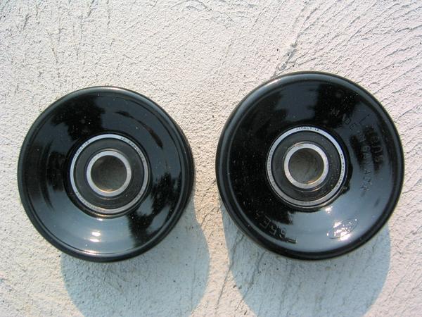 Two black idler/accessory pulleys with sealed bearings on a concrete surface