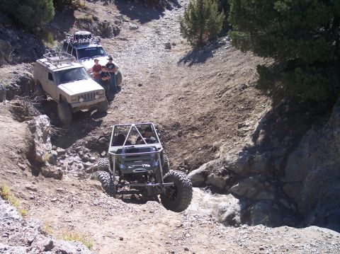 1995 Ford Bronco - Two Jeep SUVs and a custom off-road buggy navigate a rocky, dry creek bed on a sunny day. The lead Jeep is tan, while the second is white,…