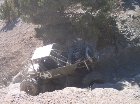 1995 Ford Bronco - A custom-built, olive green off-road buggy with a white roof is navigating a rocky, uphill terrain. The buggy has a roll cage, large tires,…