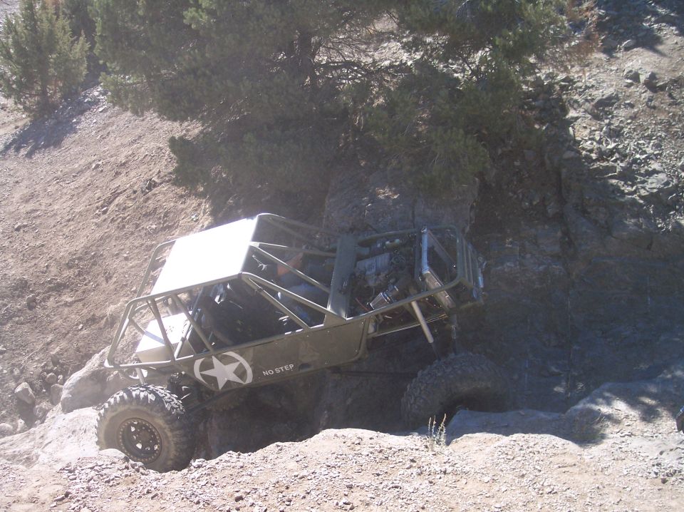 Olive green off-road buggy with white roof and star decal climbing a rocky hill.