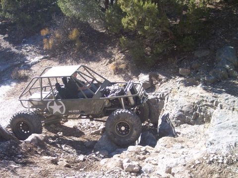 1995 Ford Bronco - A custom-built, olive drab off-road buggy with a roll cage and large tires navigates a rocky, uneven terrain.