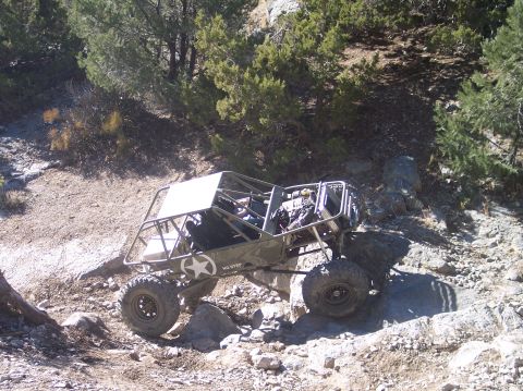 1995 Ford Bronco - A custom-built, olive green off-road buggy with a roll cage and exposed engine is navigating a rocky, uphill trail. The buggy features larg…