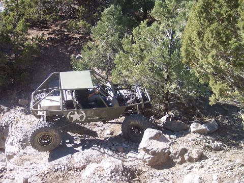 1995 Ford Bronco - A heavily modified, olive drab off-road vehicle with a roll cage and large tires is navigating a rocky, wooded hillside. The vehicle has a…