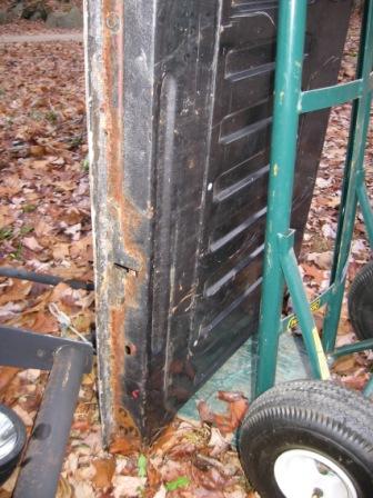 1993 Ford Bronco - Bottom edge of a removed door or panel standing on end against a green hand truck outdoors on leaf-covered ground, showing heavy surface ru…