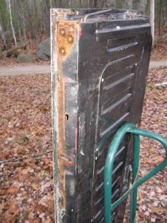 1993 Ford Bronco - A close-up, side view of a rusted and weathered black vehicle door or tailgate, possibly from a 1993 Ford Bronco, is leaning against a gree…