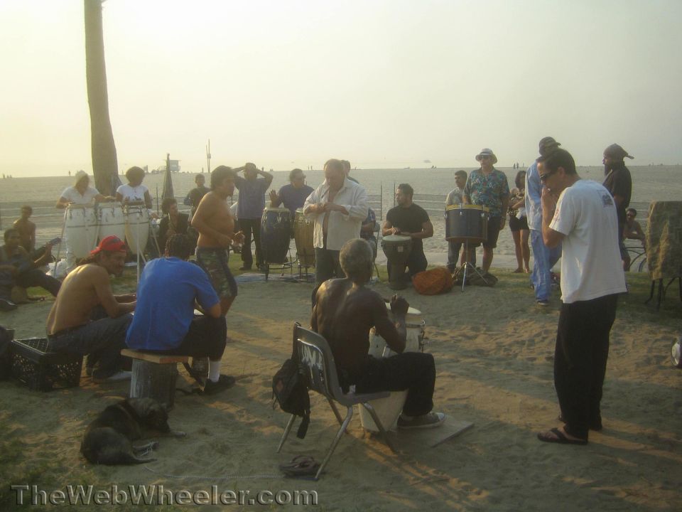 Photo of a drum circle of people gathered on the sand at dusk