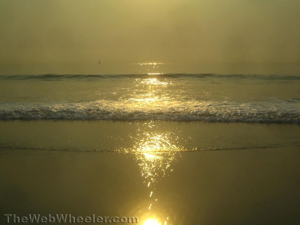 Sun setting over the ocean with waves on the beach. TheWebWheeler.com watermark visible