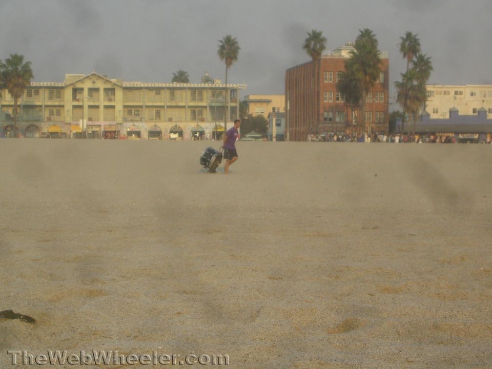 Photo of a person pulling a cart across a wide sandy beach